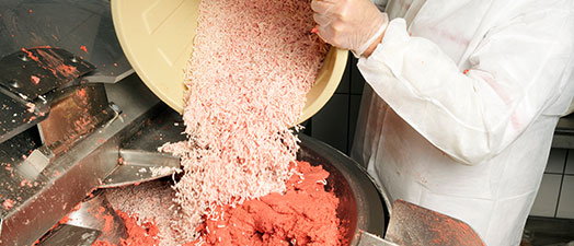 A person mixing meat in industrial machinery.